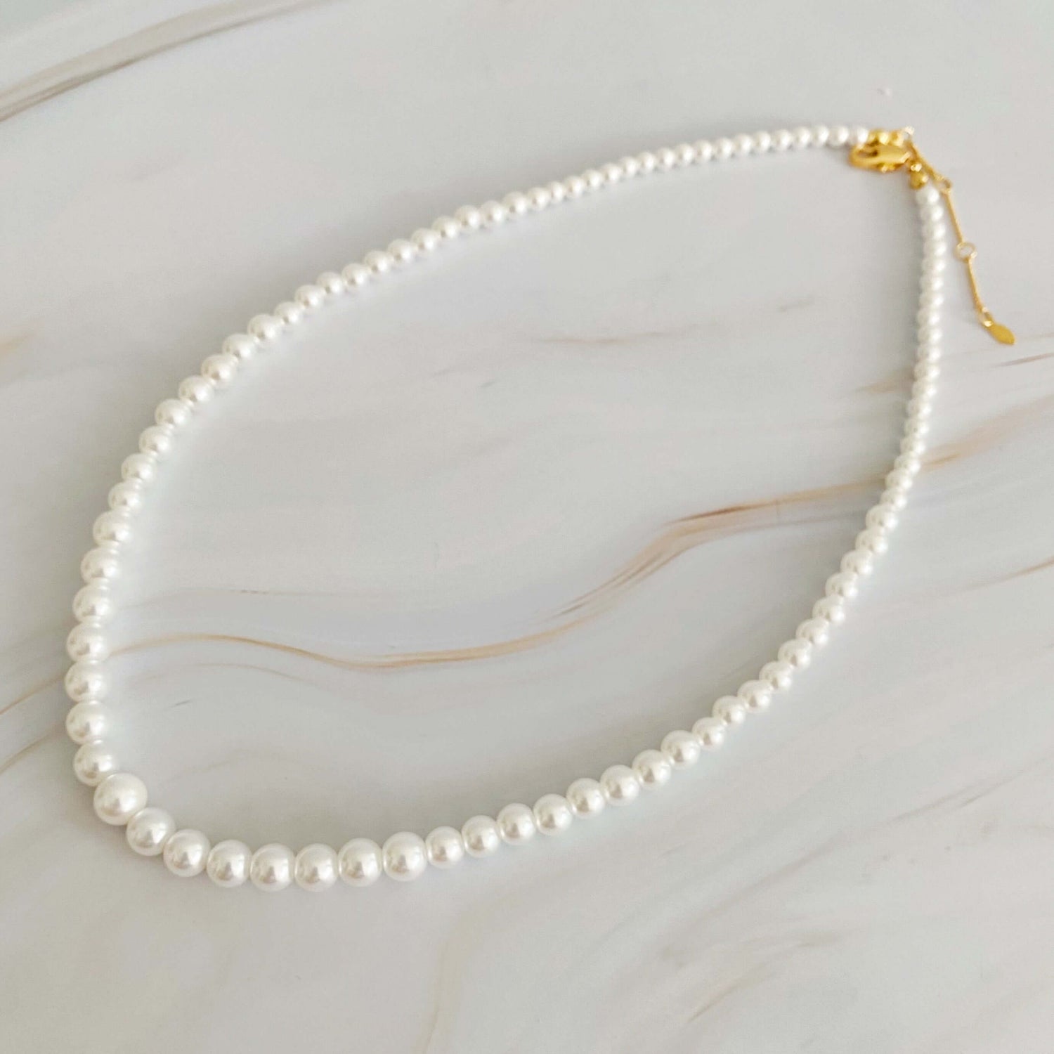 Graduated cream-toned pearl necklace with gold clasp, sizes 4mm to 7mm, ideal for layering or as a statement piece.
