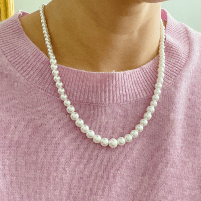 Elegant graduated pearl necklace with cream-toned glass pearls on a person wearing a pink sweater.