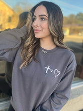 Stylish woman wearing a charcoal sweatshirt featuring a unique cross and heart design, perfect for casual wear.