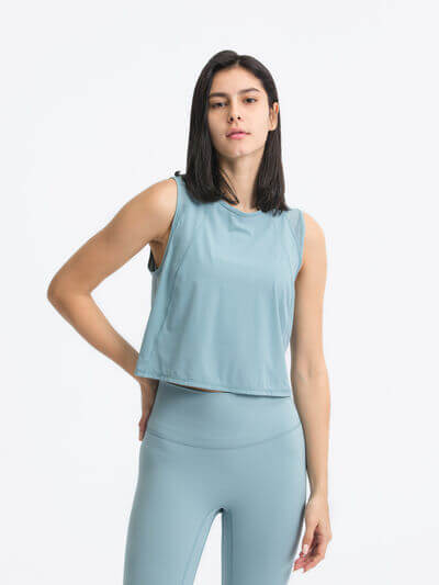 Model wearing a Millennia round neck cropped active tank in soft blue, paired with high-waisted leggings.