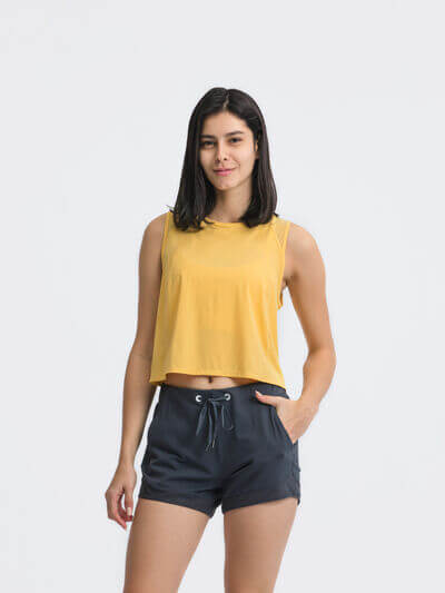 Model wearing a yellow cropped active tank top paired with navy shorts against a light background.