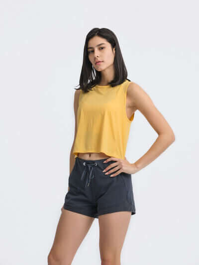 Model wearing a yellow cropped active tank top paired with dark shorts, showcasing a stylish and sporty look.