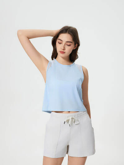 Model wearing a blue Millennia round neck cropped active tank top paired with white shorts.