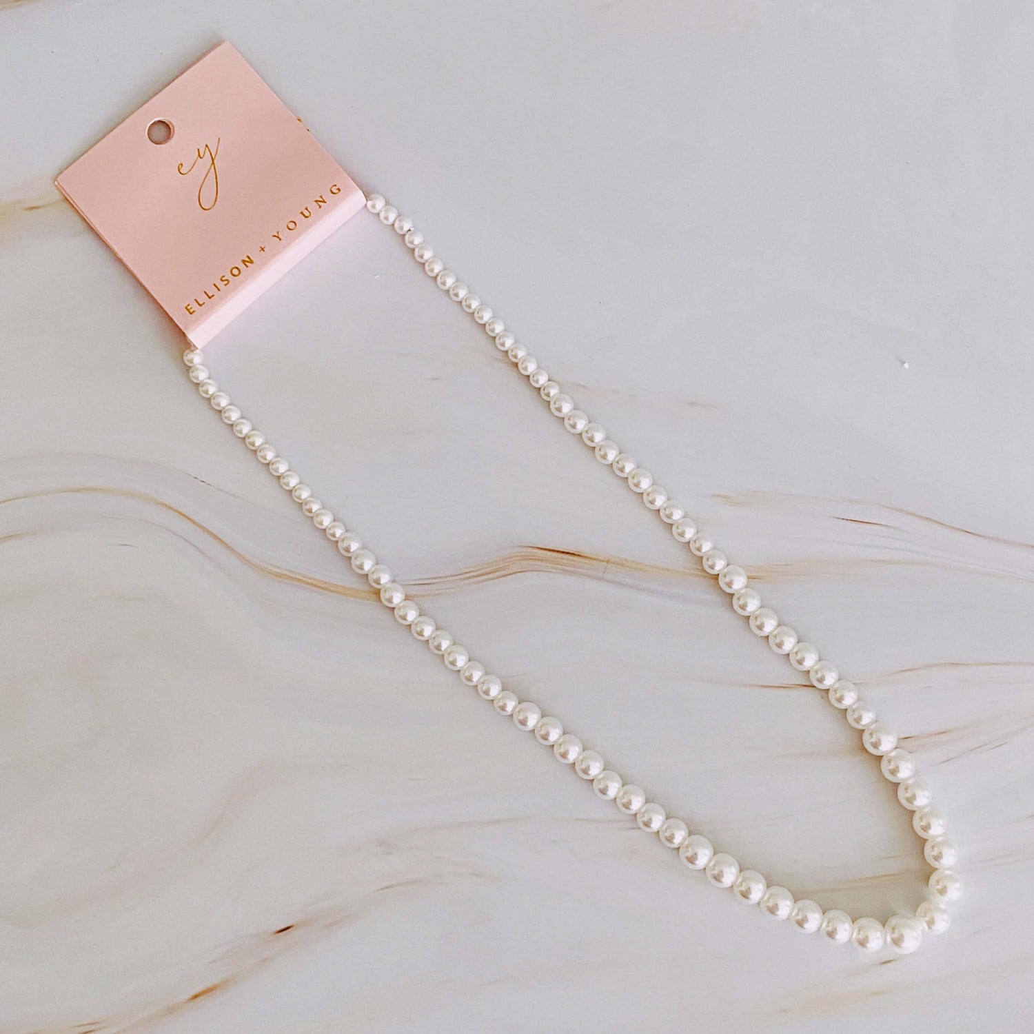 Elegant graduated pearl necklace on display with a tag, showcasing glass pearls and an 18k gold-plated clasp.