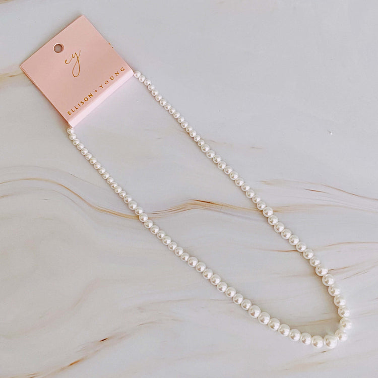 Elegant graduated pearl necklace on display with a tag, showcasing glass pearls and an 18k gold-plated clasp.