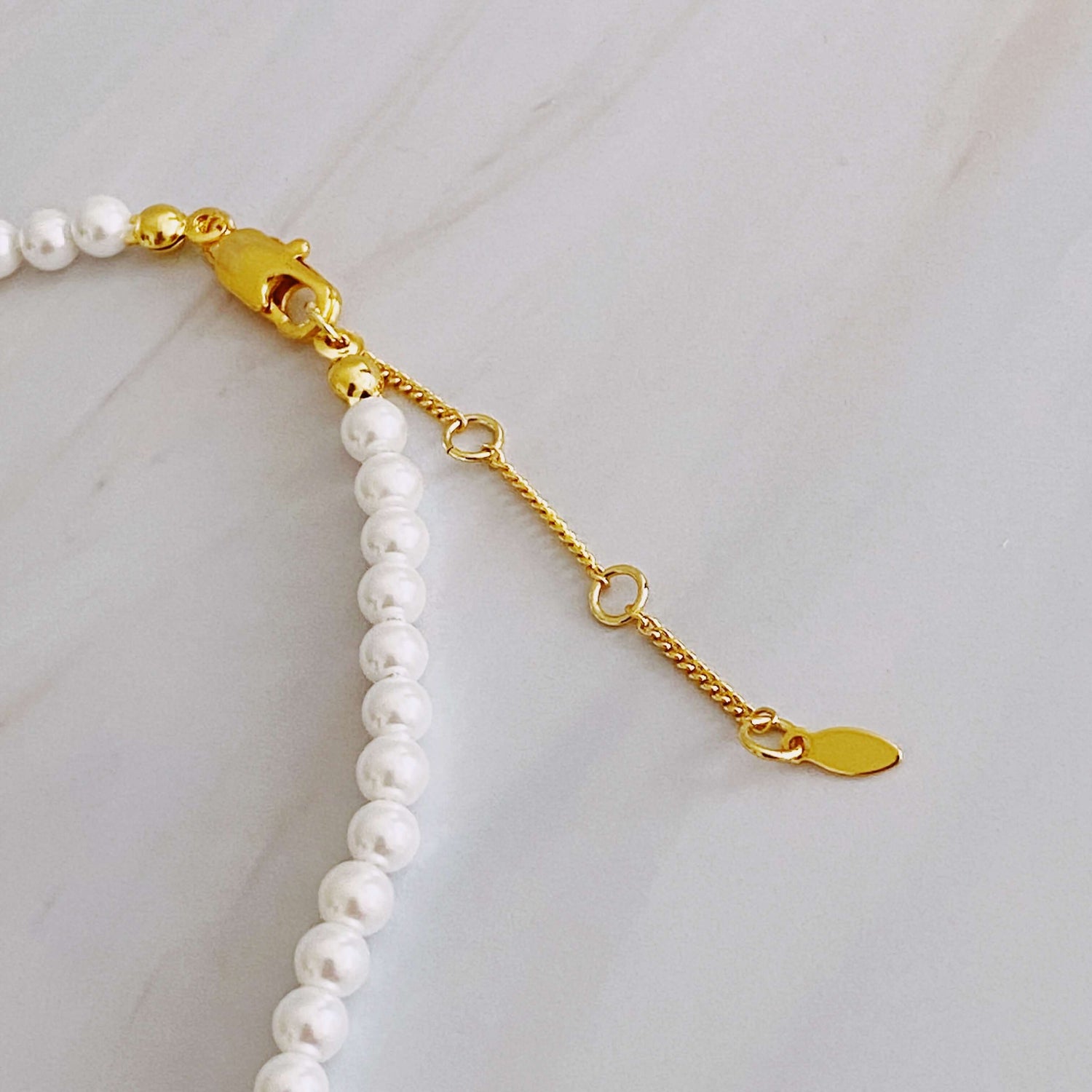 Close-up of the clasp and extender chain on a graduated pearl necklace, showcasing the gold-plated details and glass pearls.
