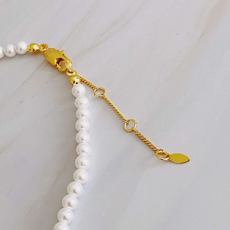 Close-up of the clasp and extender chain on a graduated pearl necklace, showcasing the gold-plated details and glass pearls.