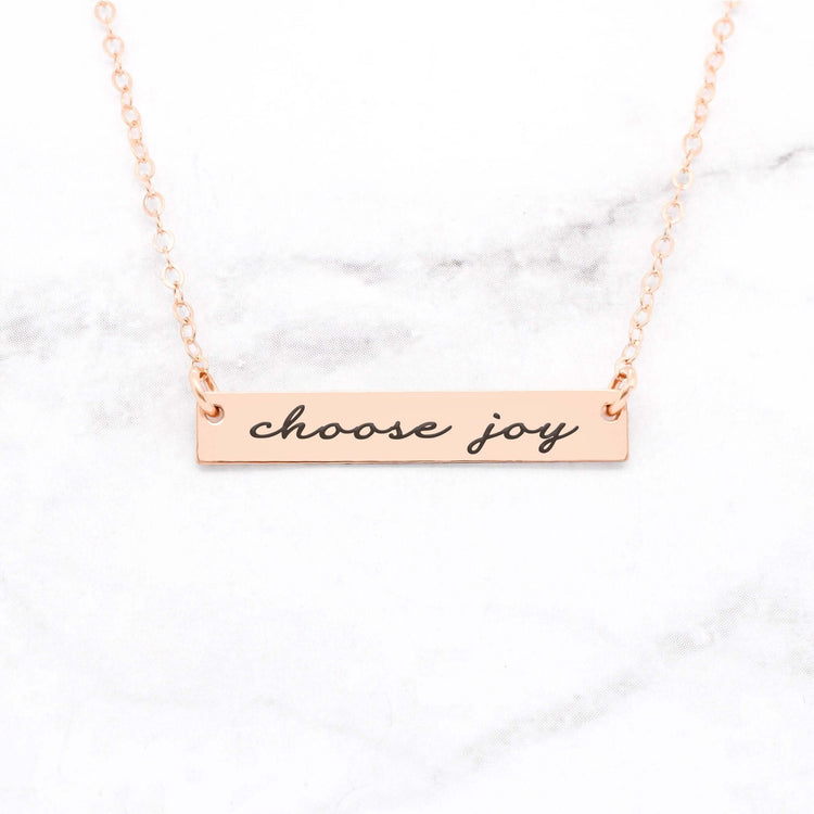 Choose Joy rose gold quote bar necklace with inspirational message on a marble background.