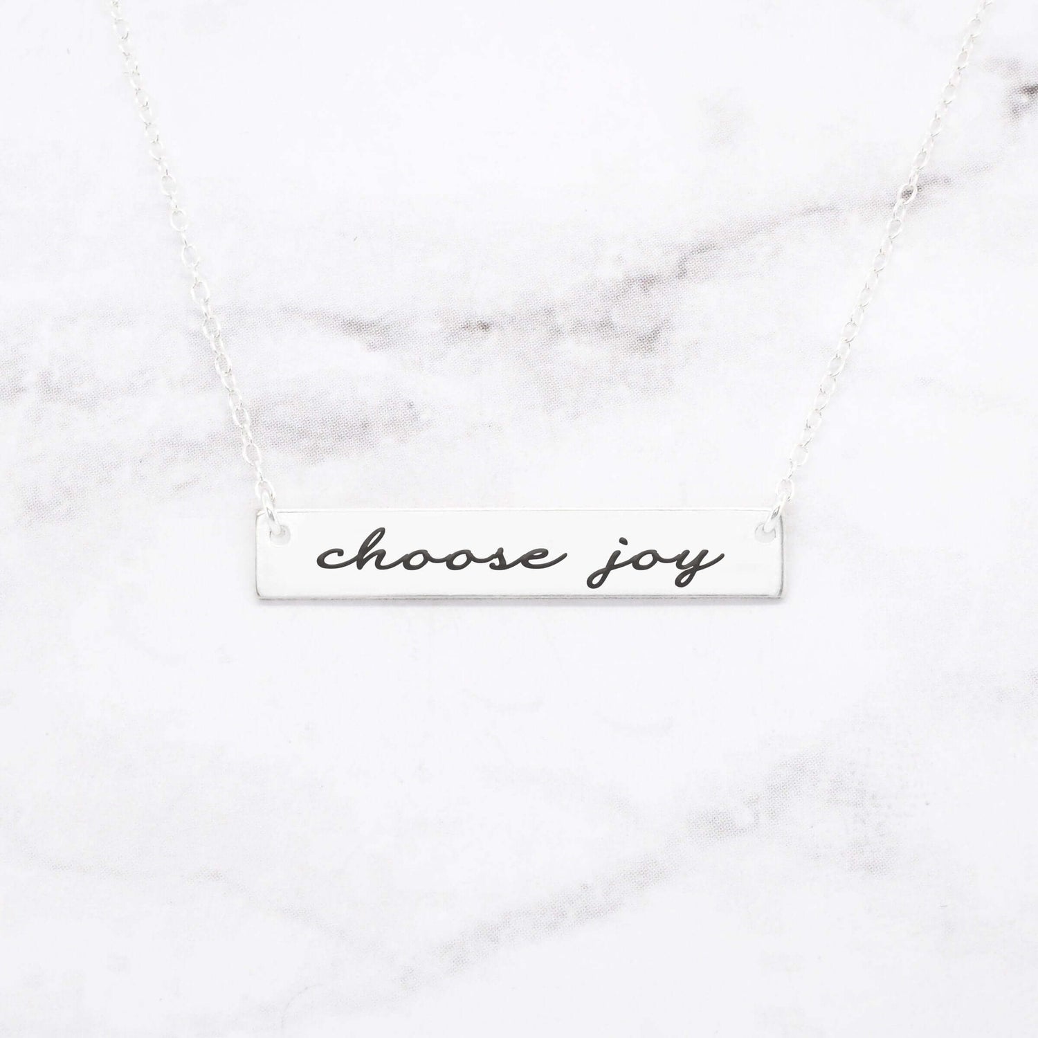 Choose Joy rose gold bar necklace featuring stylish script on a marble background.