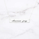 Choose Joy rose gold bar necklace featuring stylish script on a marble background.