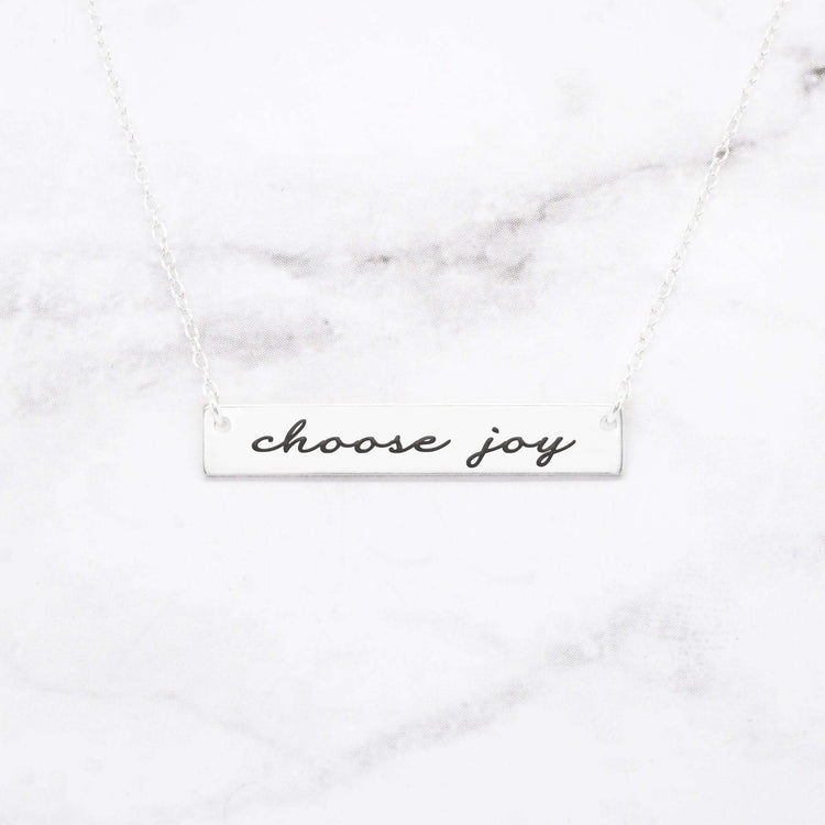 Choose Joy rose gold bar necklace featuring stylish script on a marble background.