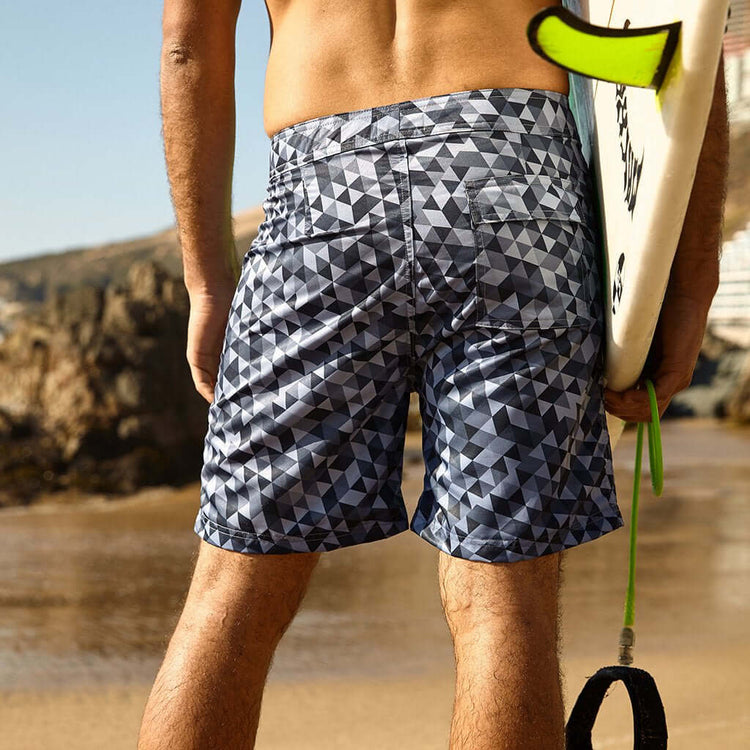 Back view of a person wearing Sustainable Surf Geometric Gray 17" Boardshorts on a beach.