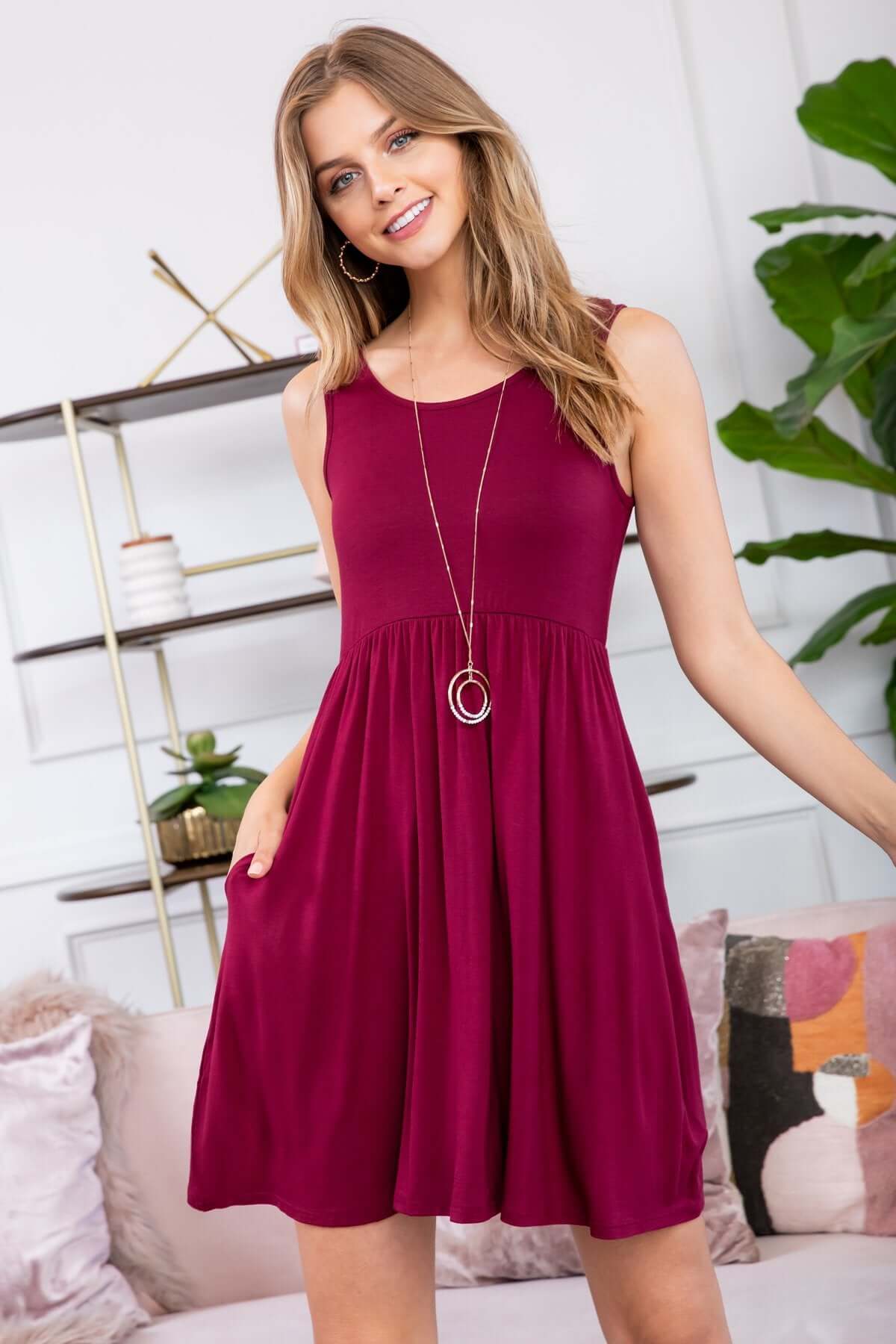 Model wearing a sleeveless burgundy racerback tank dress with pockets, styled casually for summer.