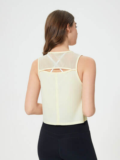 Back view of a woman wearing a Millennia Round Neck Cropped Active Tank in yellow, showcasing its sheer design and stylish fit.