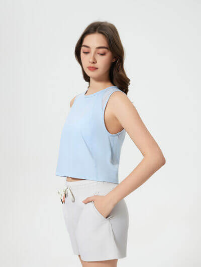 Model wearing a light blue cropped active tank top paired with white shorts, showcasing its stylish design and fit.
