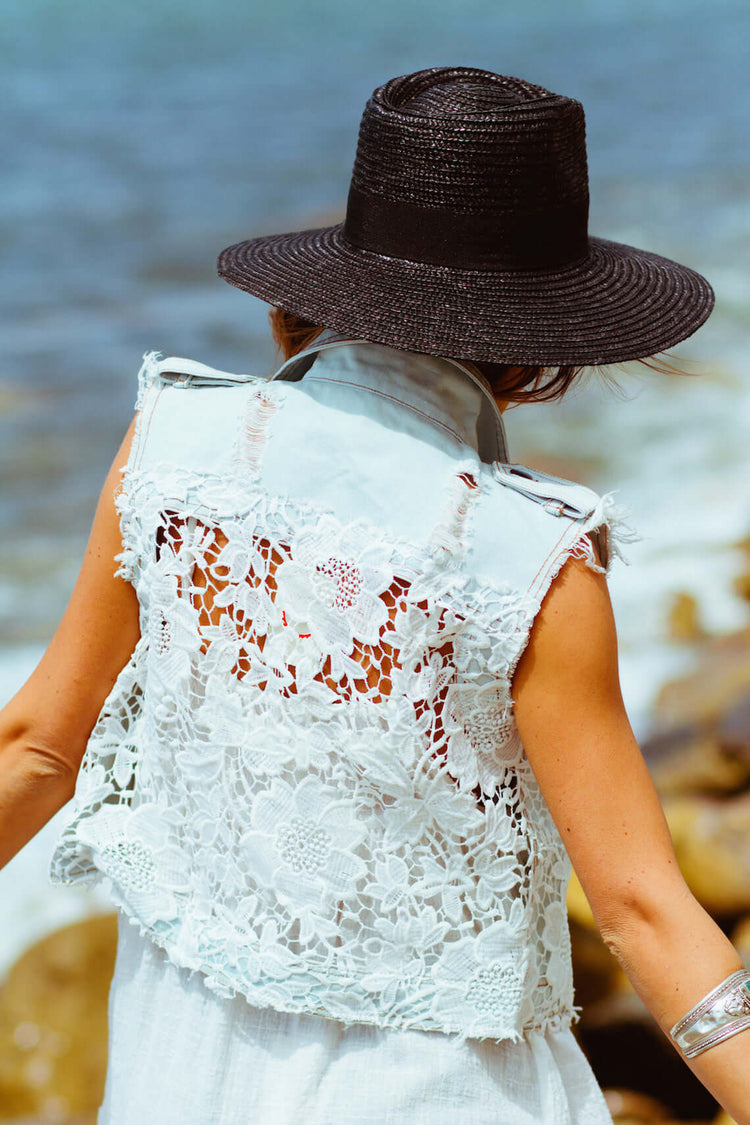Denim Margot Vest with lace back detail, styled with a black hat, perfect for summer outings by the water.