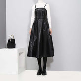 Knee-length black vegan leather dress with spaghetti straps and A-line silhouette, styled with a white turtleneck.