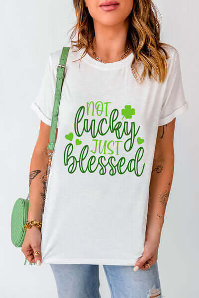 Model wearing a white round neck t-shirt featuring 'Not Lucky Just Blessed' text in green.