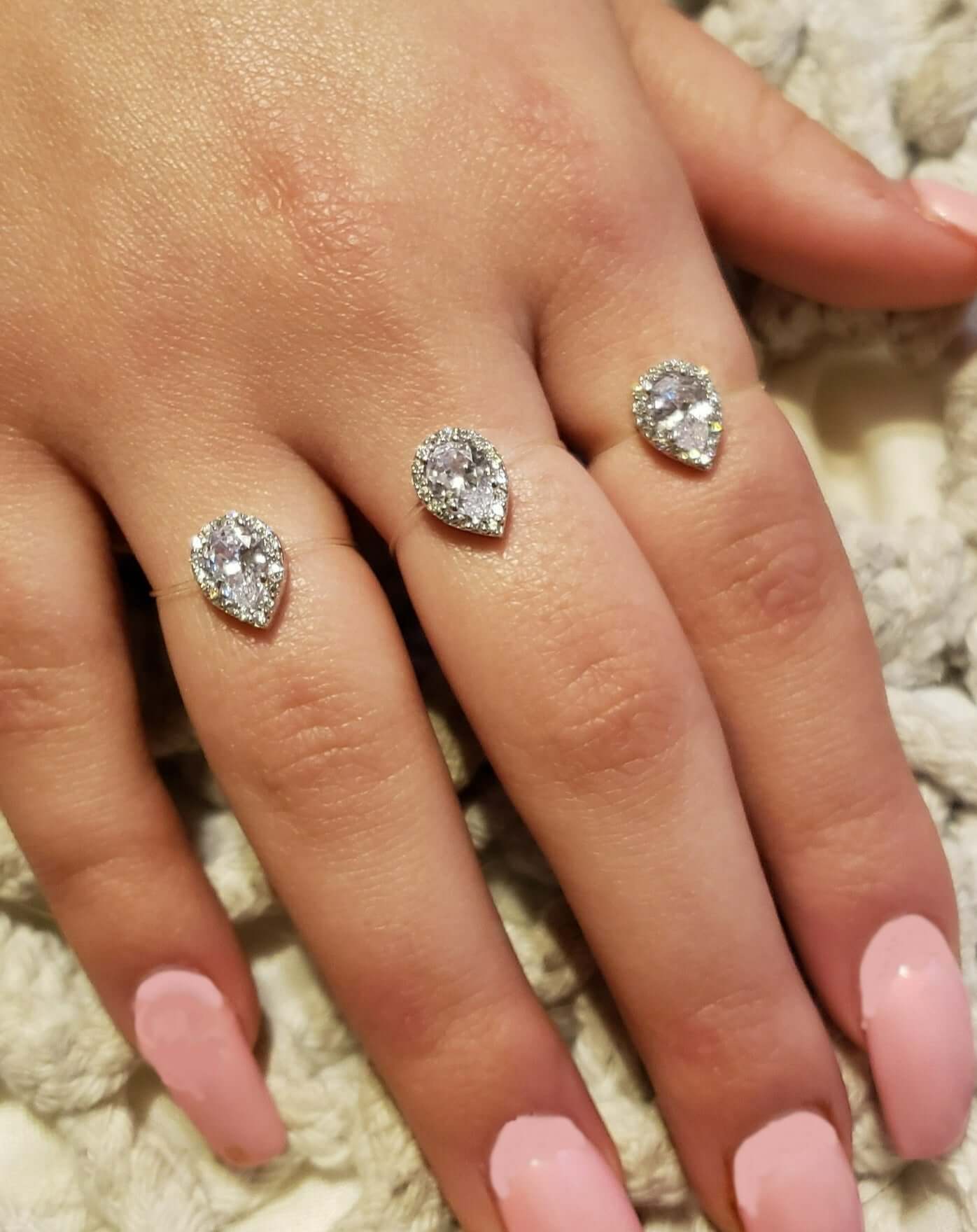 Three sterling silver pear-shaped rings with cubic zirconia on a hand with pink nails, showcasing a floating diamond illusion.