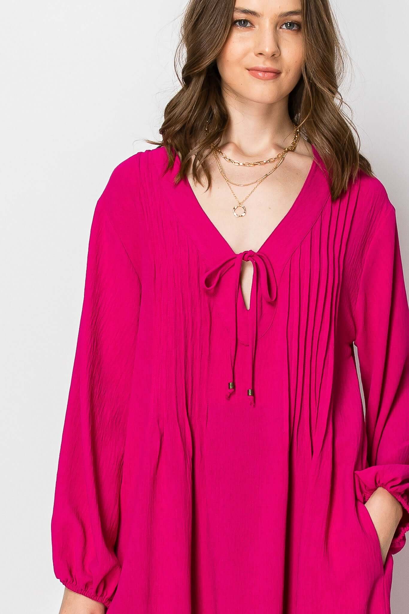 Long sleeve pintuck A-line dress in bright pink with V-neck and front tie, perfect for casual fall outfits.