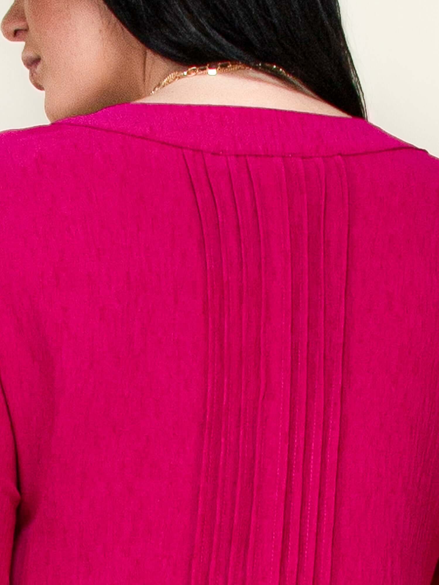 Close-up of pintuck detailing on the back of a long sleeve pink dress, showcasing elegant texture and style.