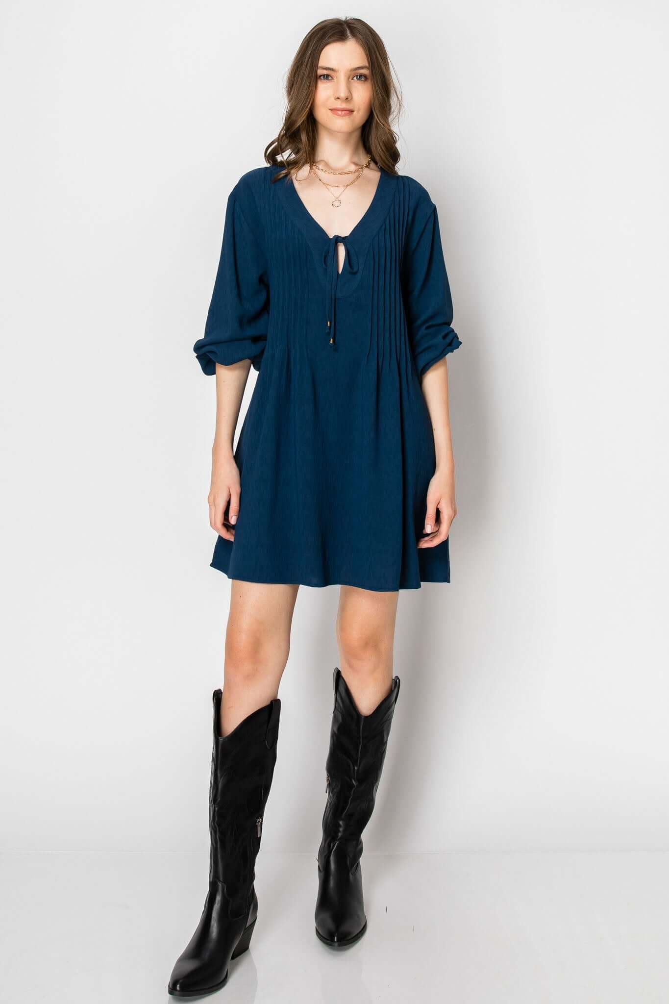 Long sleeve pintuck A-line dress in teal with front tie, styled with black western boots, perfect for fall attire.