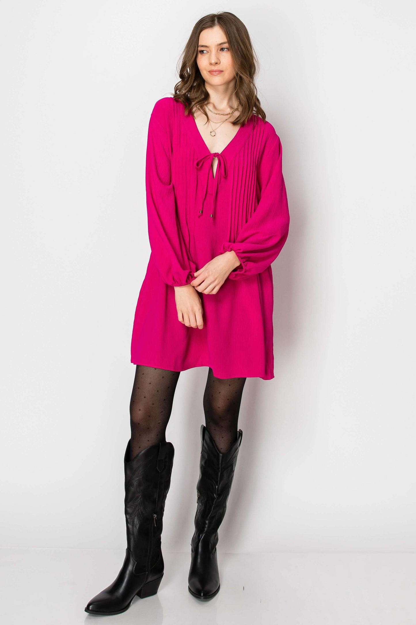 Model wearing a hot pink long sleeve pintuck A-line dress with front tie and pockets, styled with black western boots.