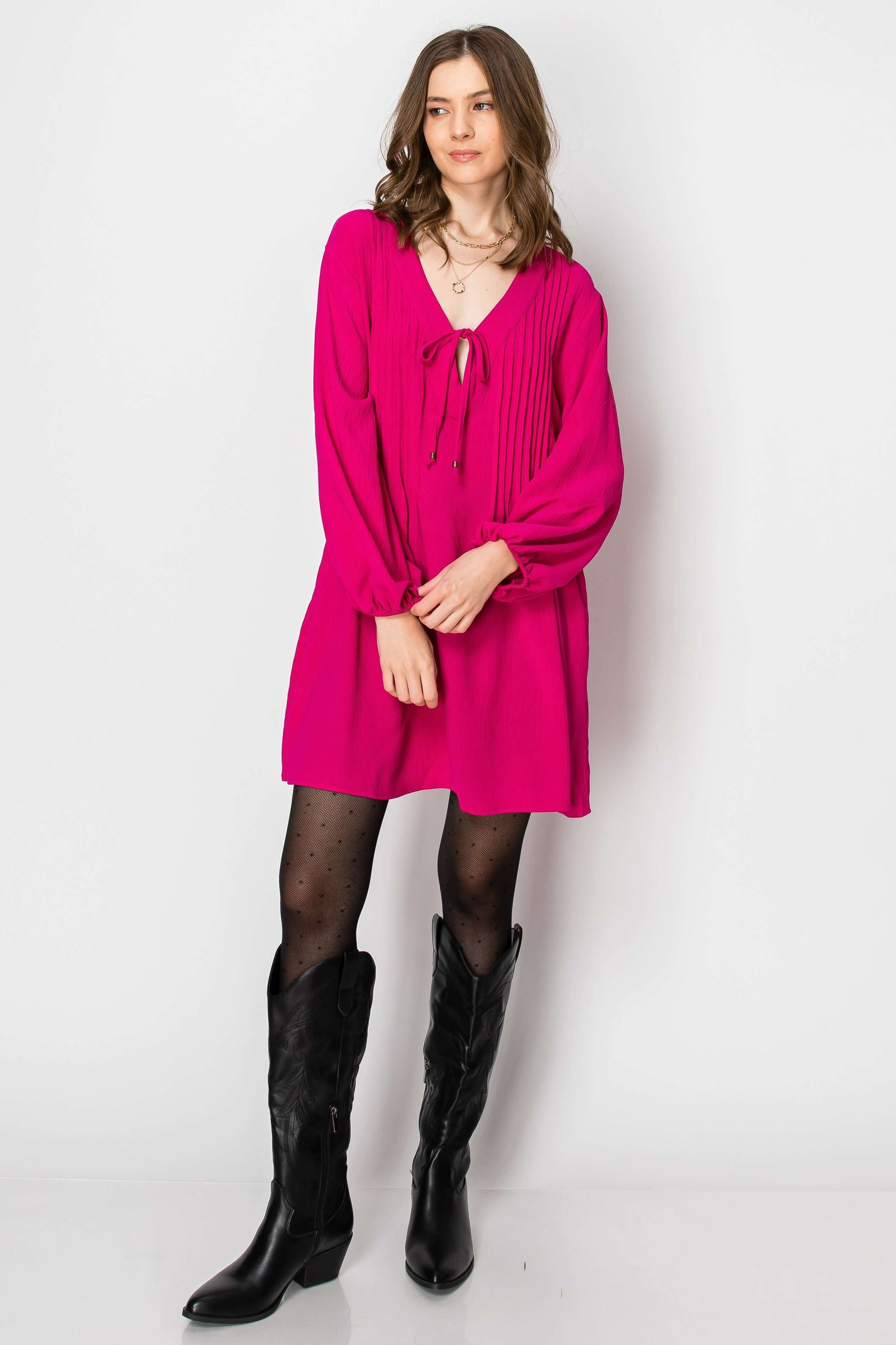 Model wearing a hot pink long sleeve pintuck A-line dress with front tie and pockets, styled with black western boots.