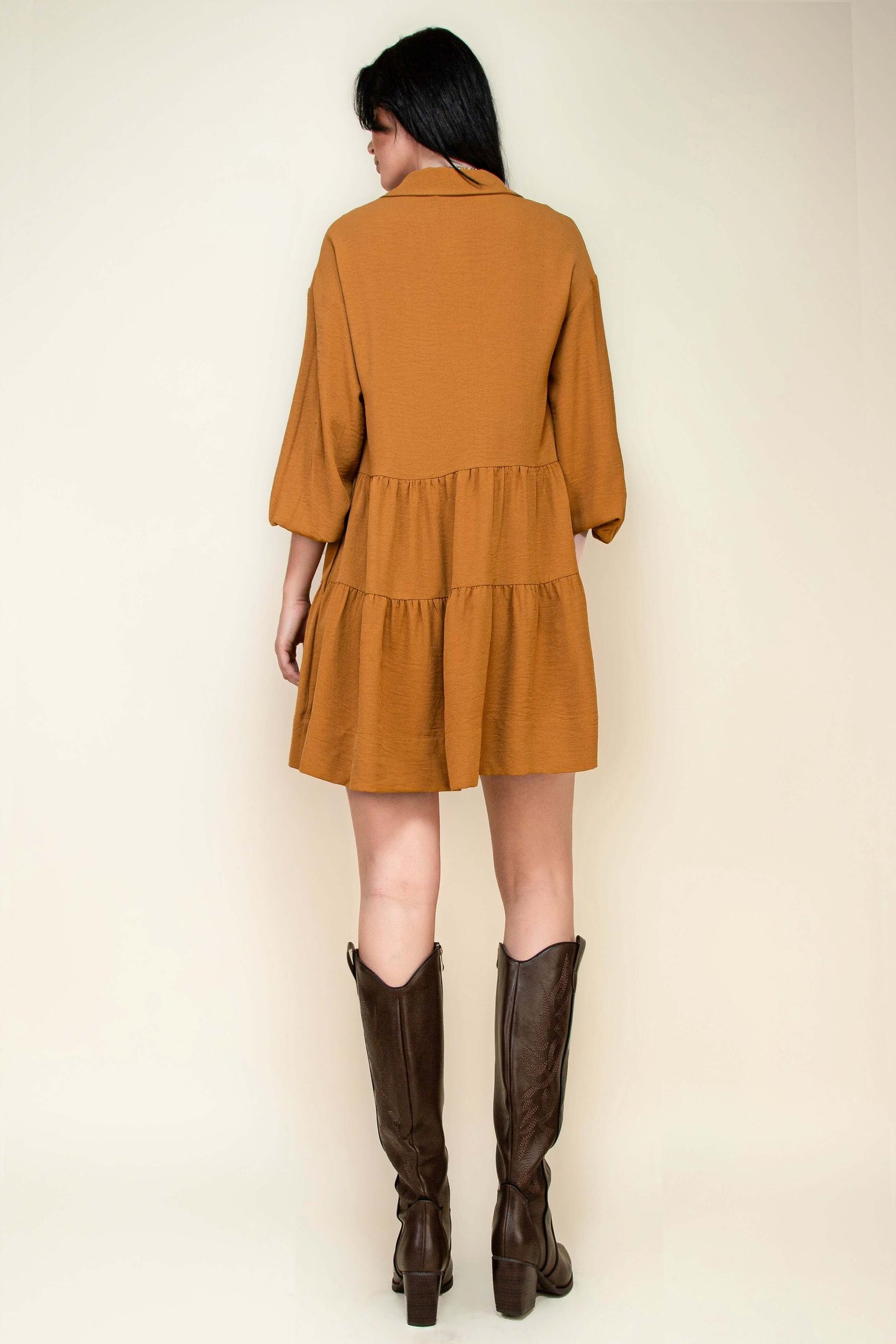 Back view of a flowy long sleeve collared button-down tiered ruffle dress in mustard, styled with brown western boots.