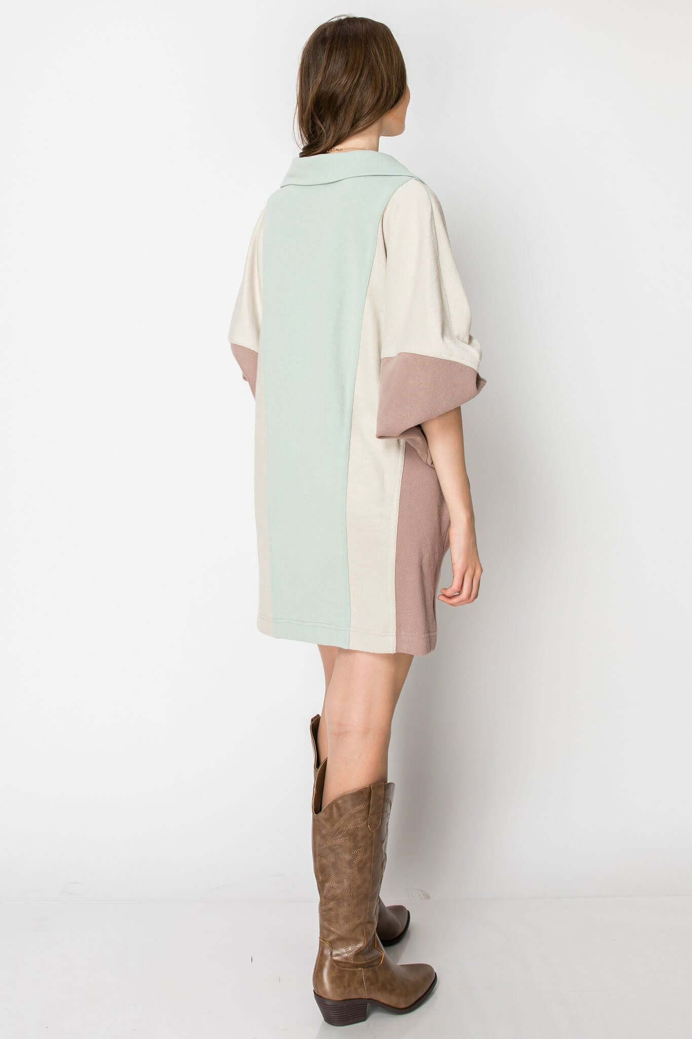 Back view of a color block long sleeve collared mini dress in soft fall colors, paired with brown western boots.