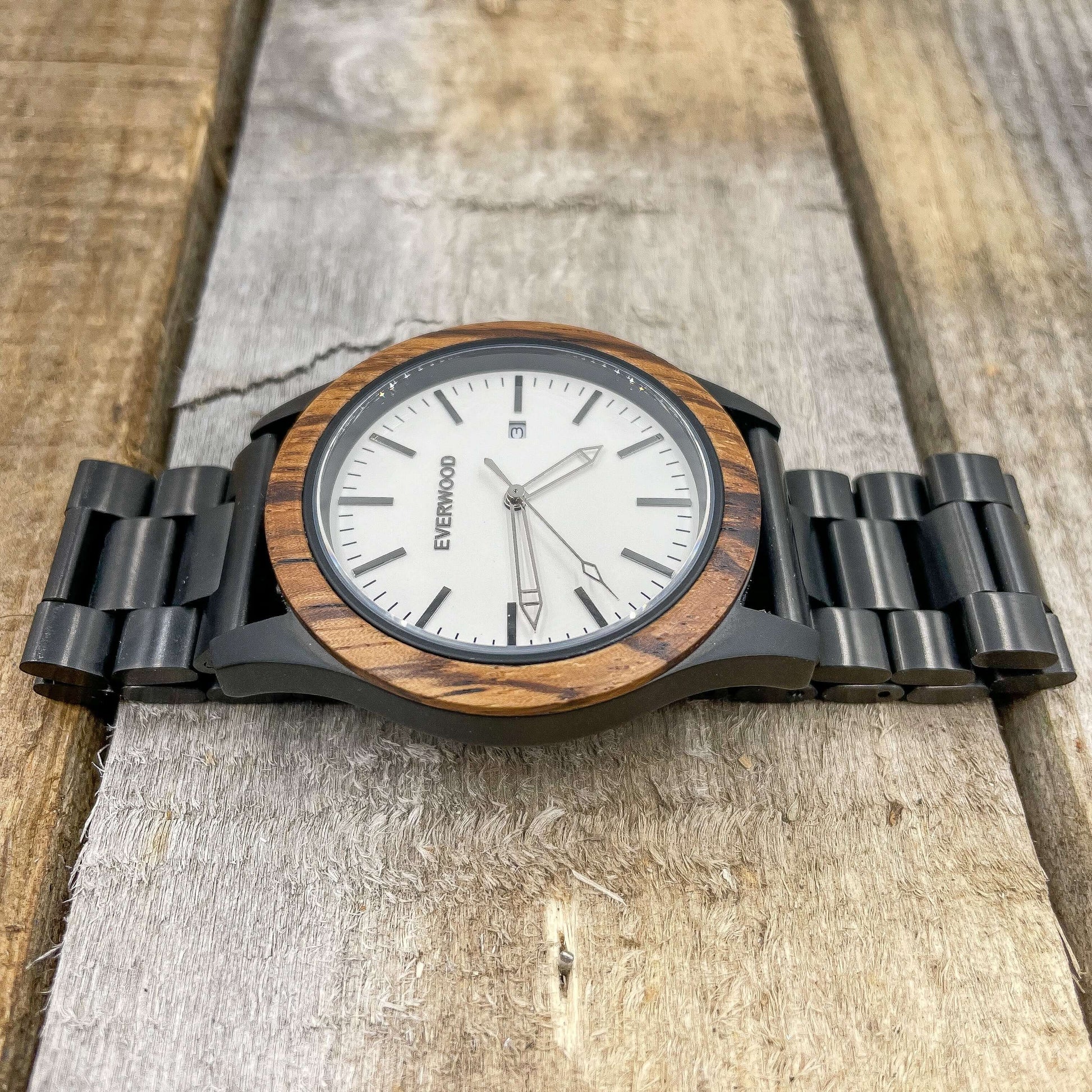 Inverness SS watch with Zebrawood bezel, Miyota quartz movement, stainless steel strap, and mineral crystal on wooden surface.