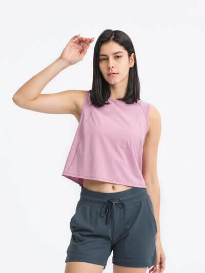 Model wearing a pink cropped active tank with a round neck, paired with dark shorts.