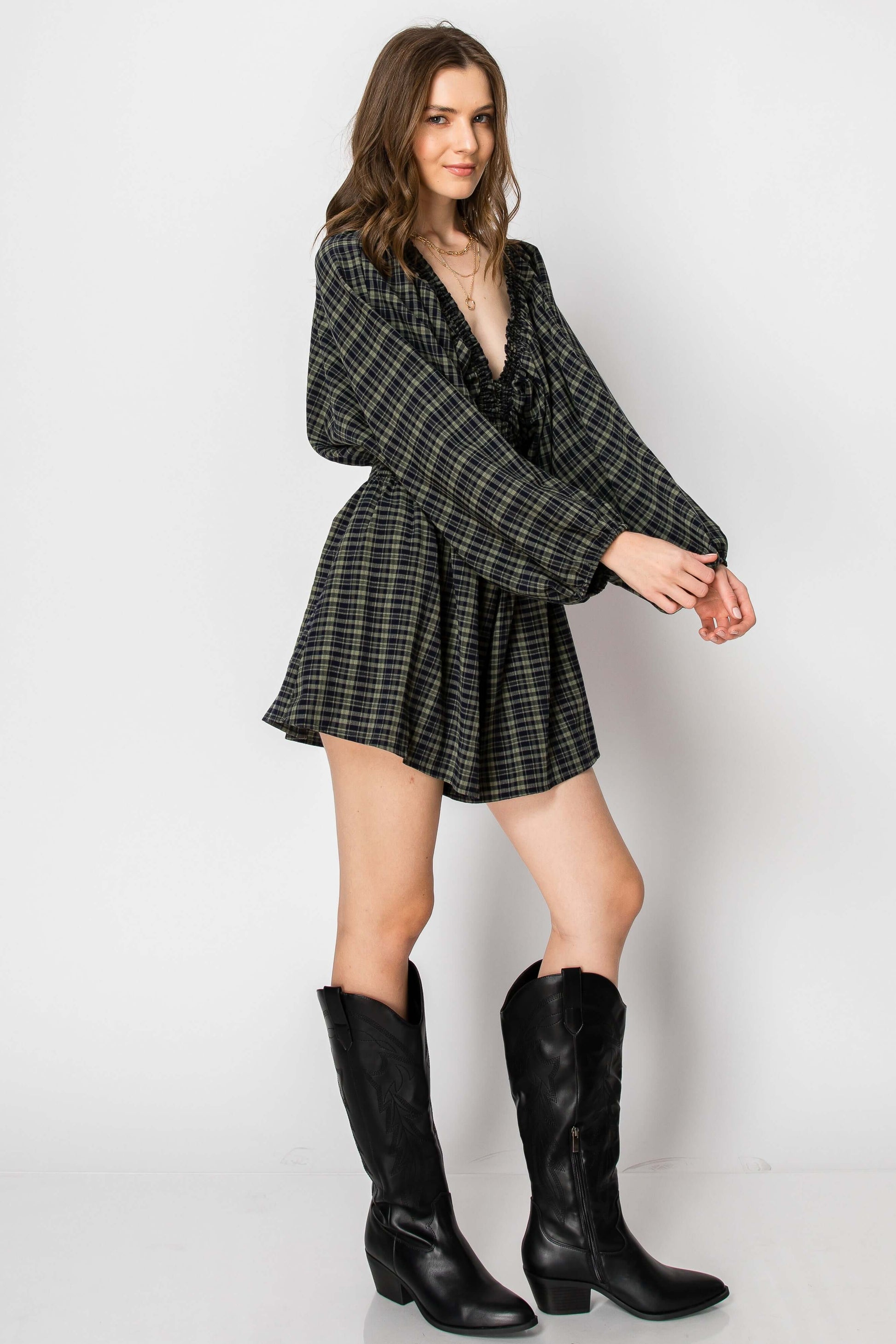 Model wearing Dolman Sleeve Plaid Smocked Deep V Neck Romper with pockets and balloon sleeves, styled with black boots.