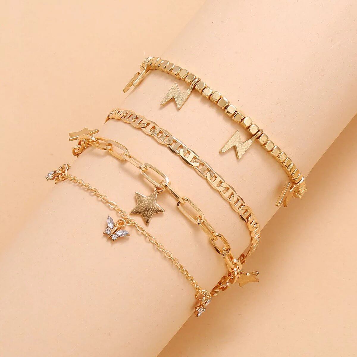 Trendy gold plated anklet set with four adjustable pieces on a wrist, featuring charming star and butterfly designs.