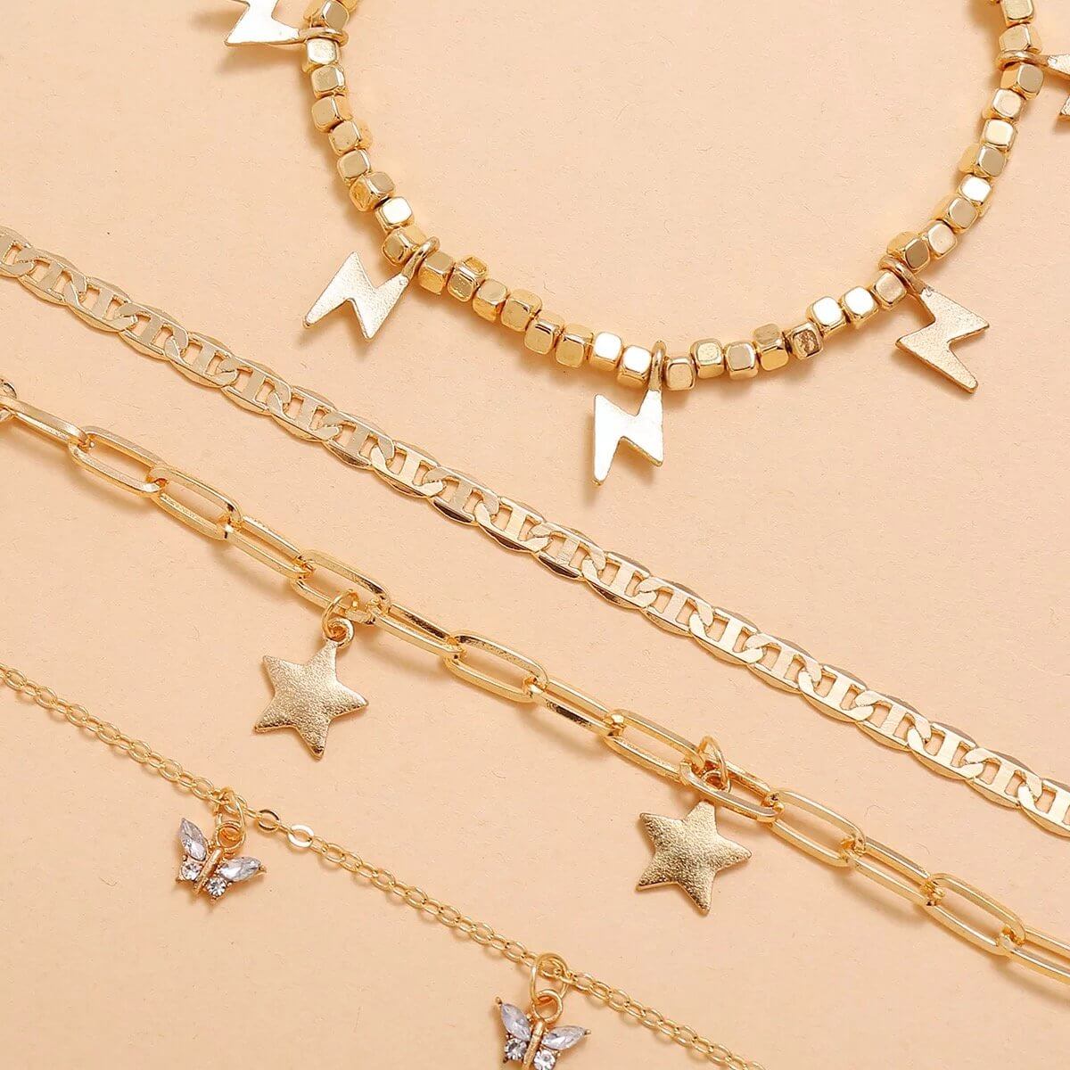 Trendy Player Anklet Set featuring gold plated anklets with lightning bolts, stars, and butterflies on a beige background.