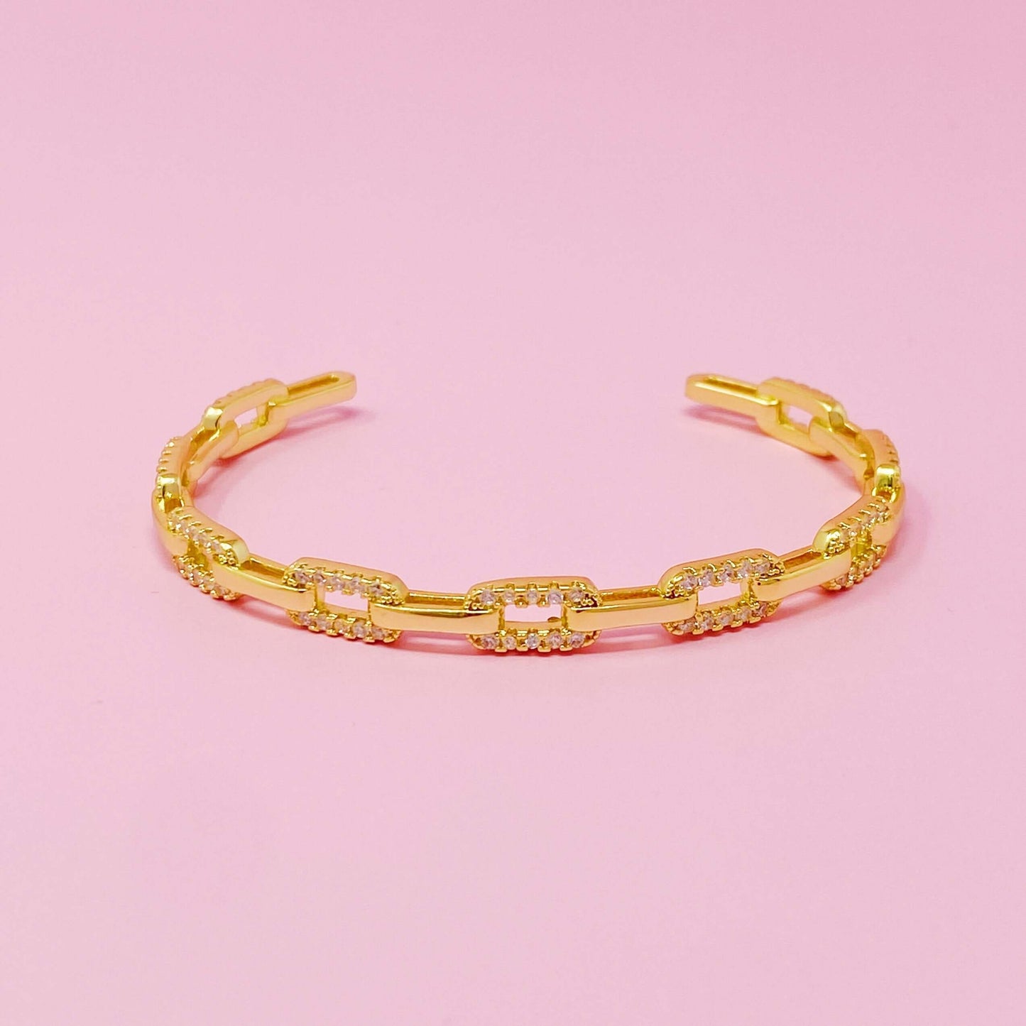 Stylish alternatively linked open bangle bracelet in 18k gold plated brass with cubic zirconia on pink background.