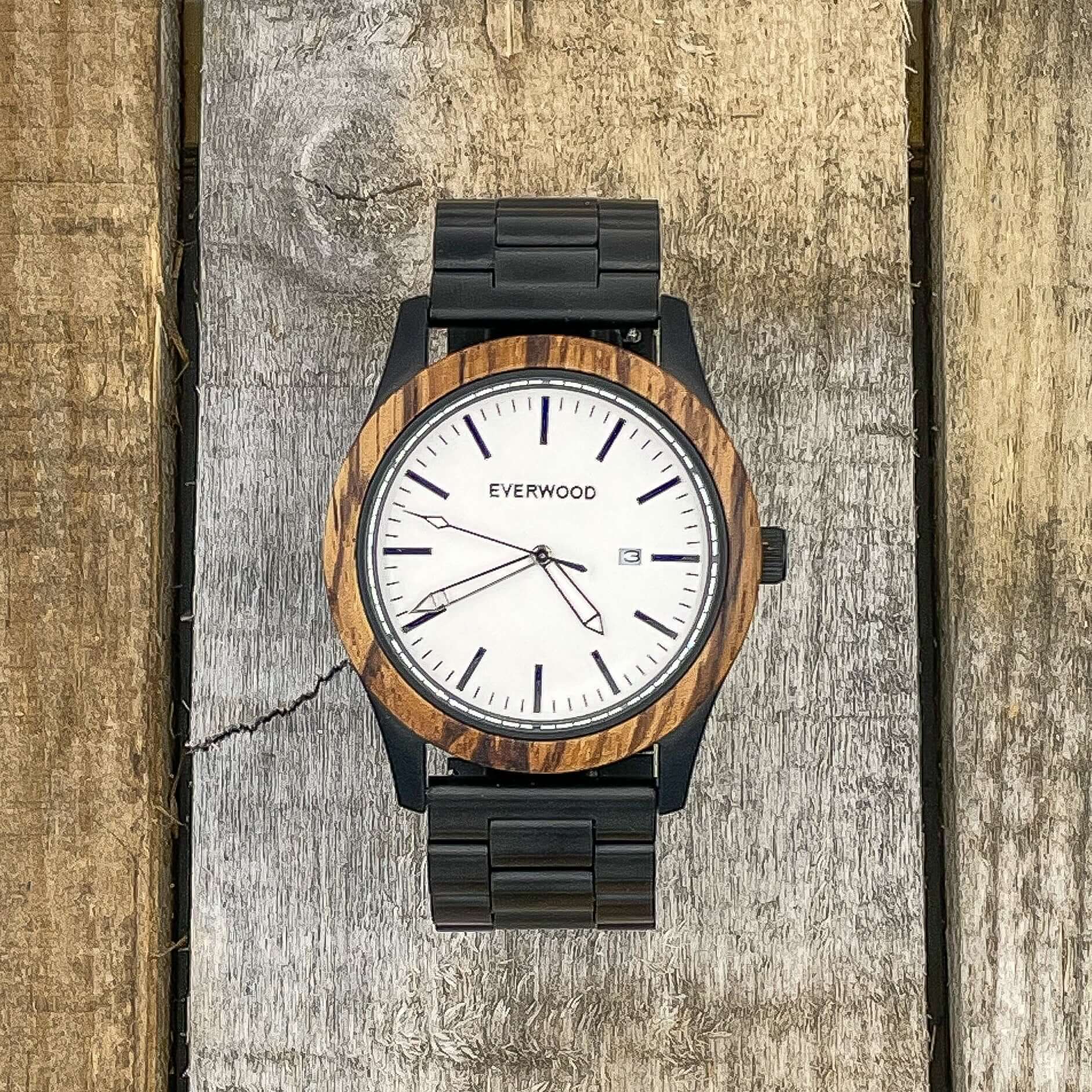 Inverness SS watch featuring a zebrawood bezel, white dial, Miyota quartz movement, and stainless steel strap on wooden background.