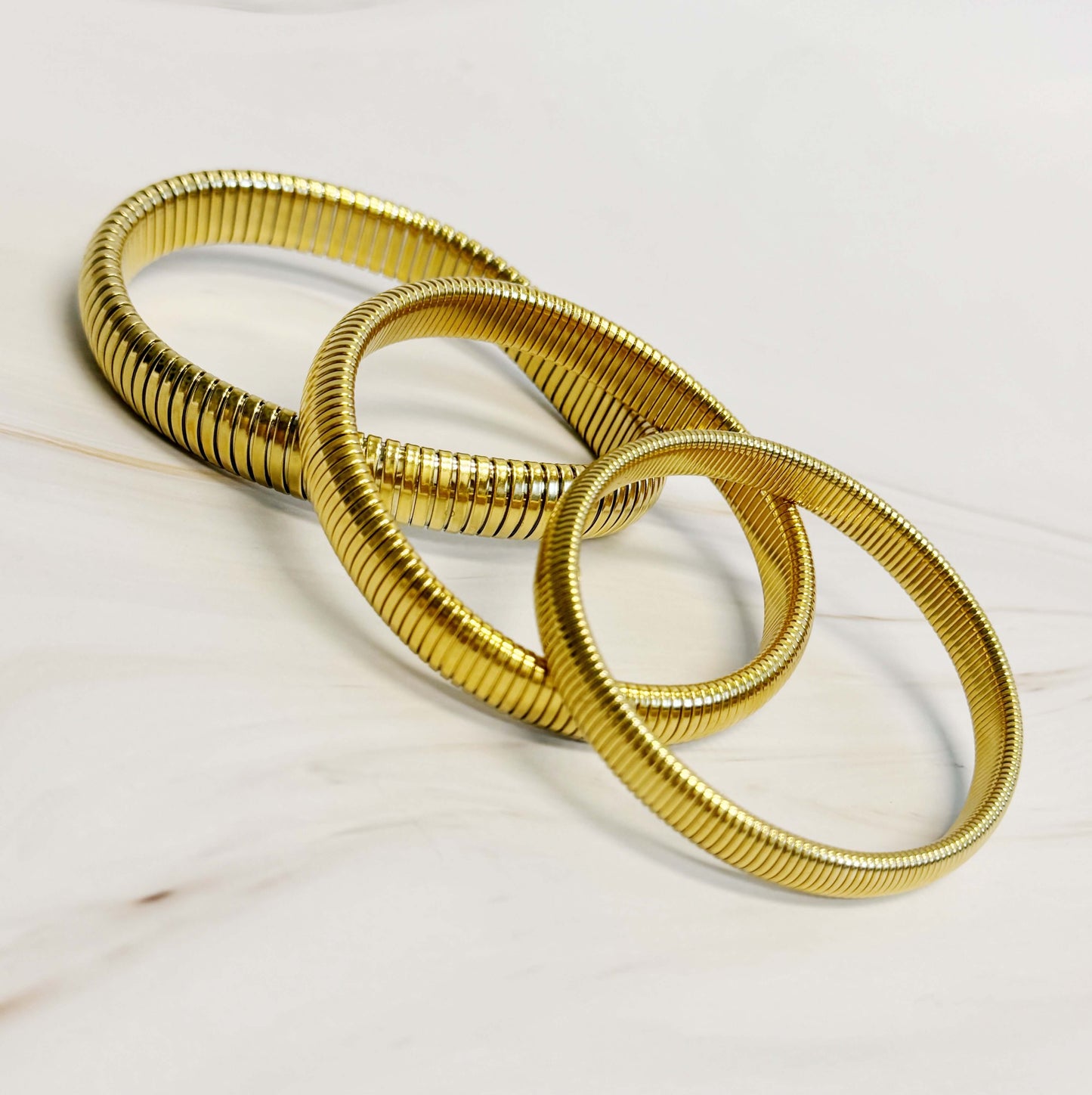 Three golden spring soft bangle bracelets on a marble surface, showcasing stylish design and comfortable texture.