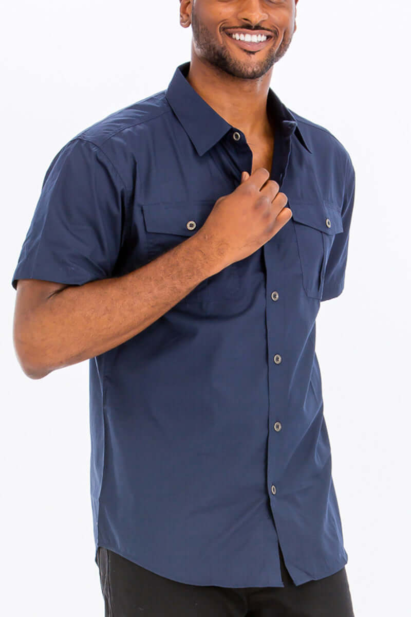 Man wearing a navy blue short sleeve two pocket button down shirt with branded buttons and dual chest pockets.