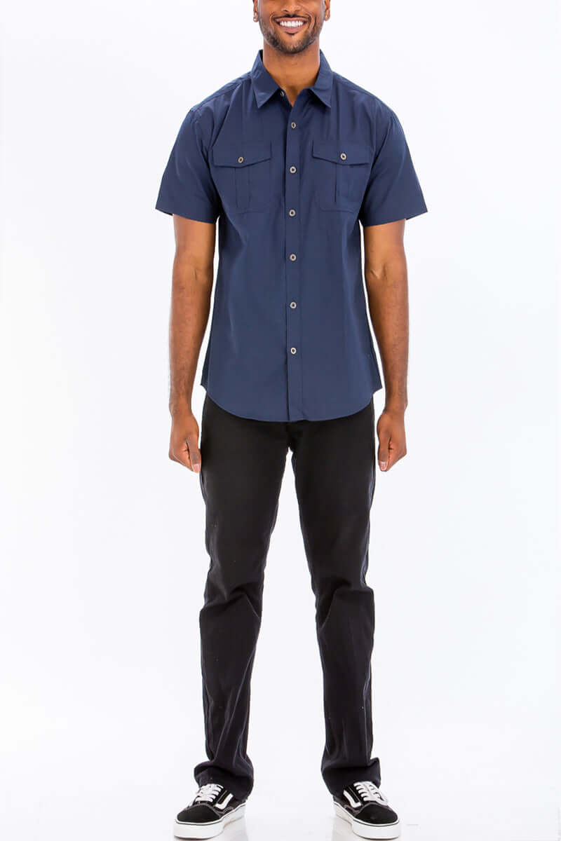 Model wearing a navy blue short sleeve button down shirt with dual chest pockets and branded buttons.