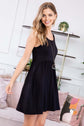 Woman modeling a black racerback tank dress with a flared silhouette and pockets, styled in a chic setting.
