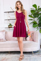 Model wearing a burgundy racerback tank dress with pockets, styled with wedges in a modern living room setting.