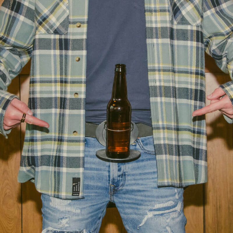 Man wearing plaid shirt with 'Merica Belt Buckle holding a beer bottle, showcasing fun American tradition.