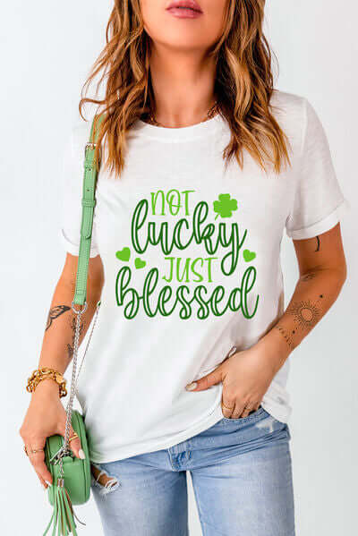 Model wearing a white 'Not Lucky Just Blessed' round neck T-shirt with green text, styled casually with jeans.