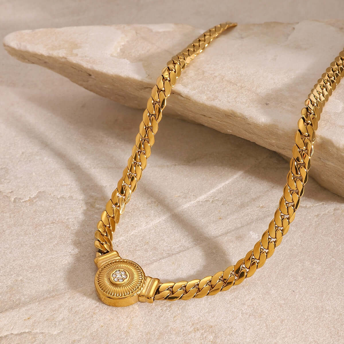 Close-up of a luxurious gold necklace with a diamond-studded pendant on a stone surface.