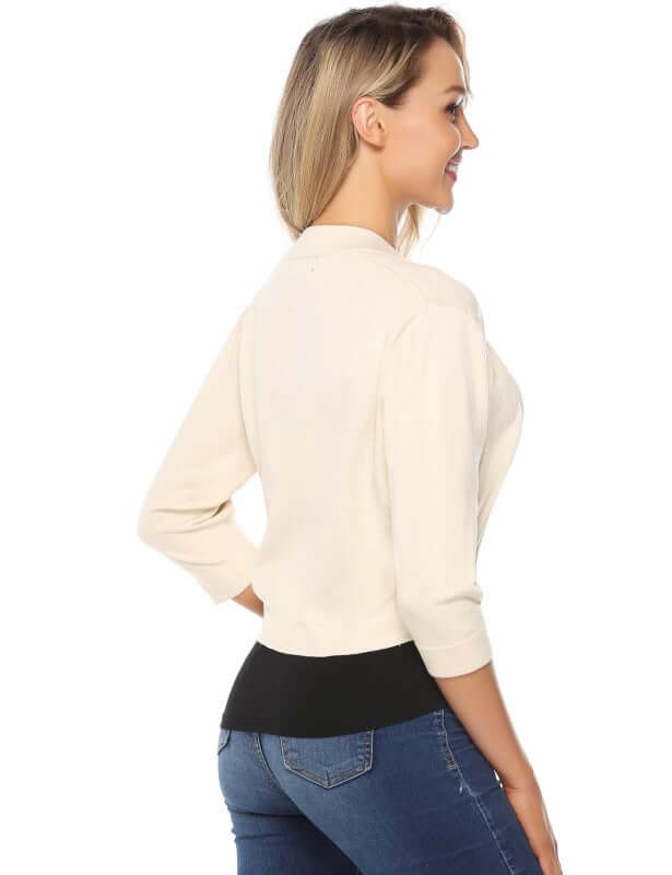 Woman showcasing a back view of a cream 3/4 sleeve cropped cardigan styled with jeans.