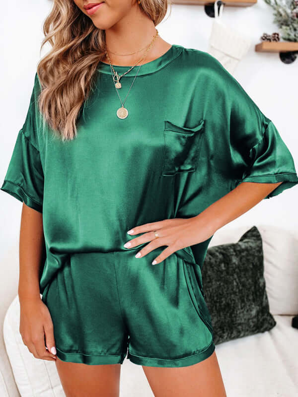 Women's satin pajamas in green, short-sleeved top and shorts, featuring a pocket and dropped shoulder sleeves.