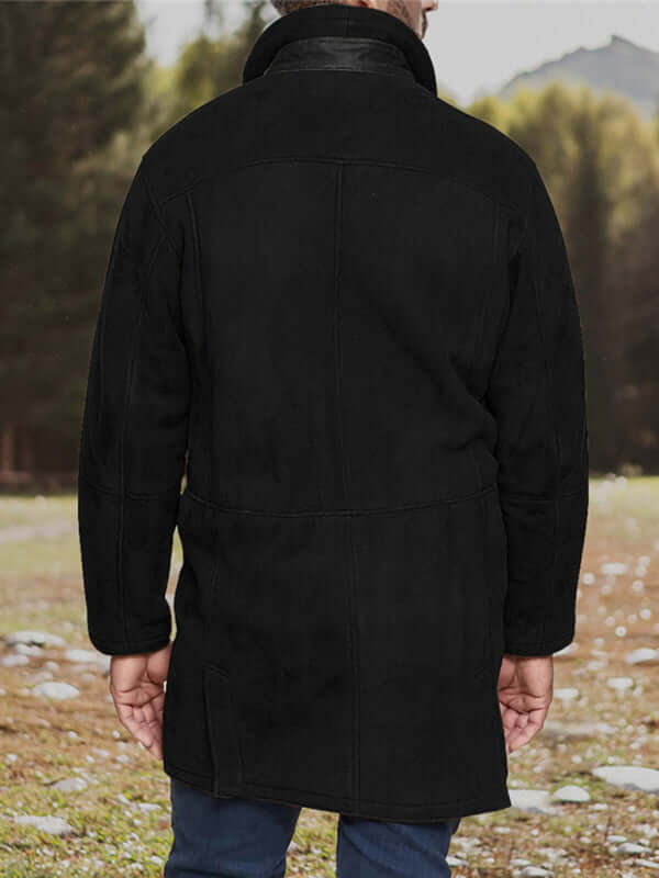 Men's mid-length black woolen coat with a zipper, viewed from the back, in a natural outdoor setting.