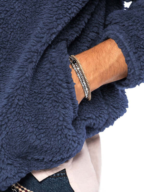 Close-up of a hand wearing a stylish bracelet, showcasing a cozy navy blue jacket with a textured fleece finish.