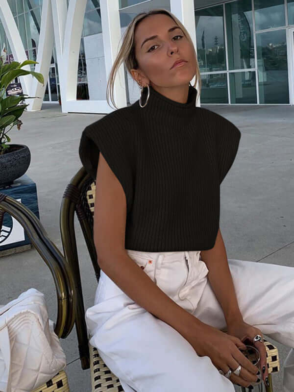 Women wearing a black turtleneck short-sleeved sweater top, styled casually with white pants in a modern setting.